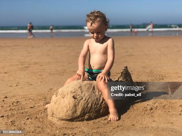 boy toddler sitting on a fish sand sculpture at beach buzios - speedo boy stock pictures, royalty-free photos & images