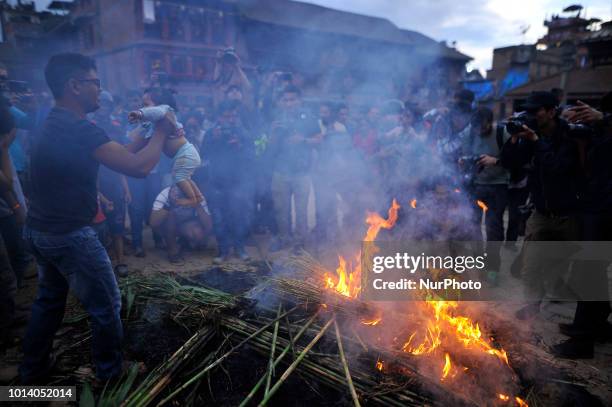 Nepalese devotee swing their child over the burning straw effigy of the demon Ghantakarna during the Gathemangal festival celebrated at Bhaktapur,...