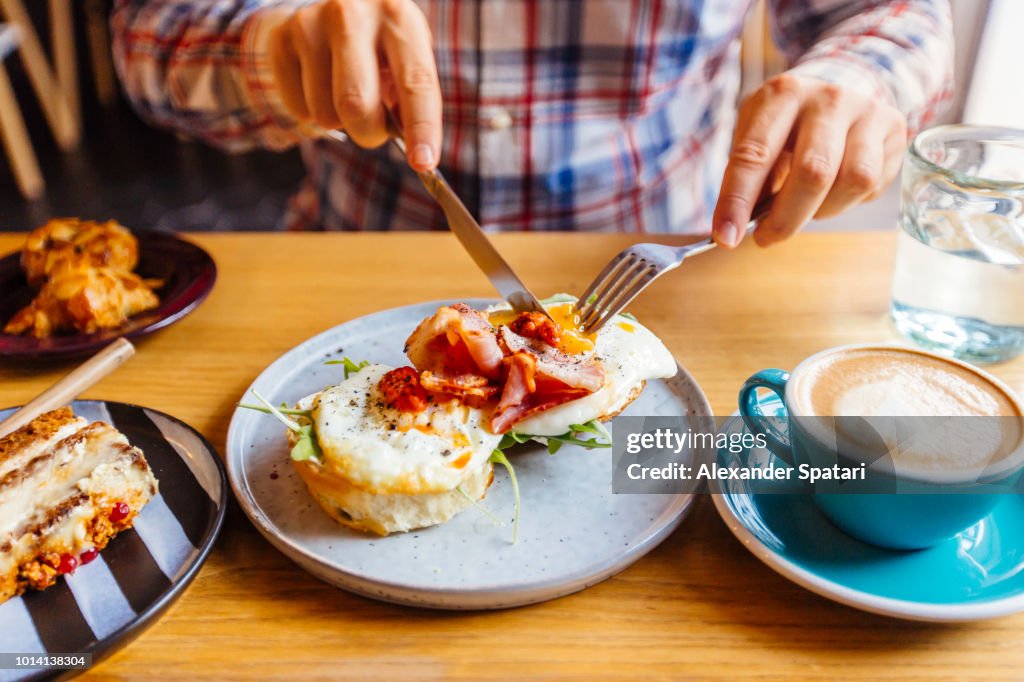 Man eating breakfast with egg, bacon, arugula on brioche bun and coffee