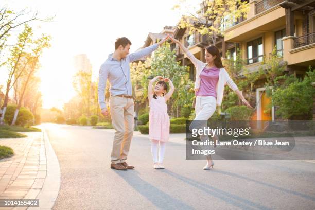 happy young family standing in front of their new house - dreiviertel vorderansicht stock-fotos und bilder