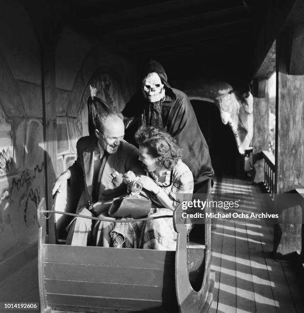 Man in a skeleton costume looms over two passengers on the Ghost Train at a fairground, 16th May 1952.