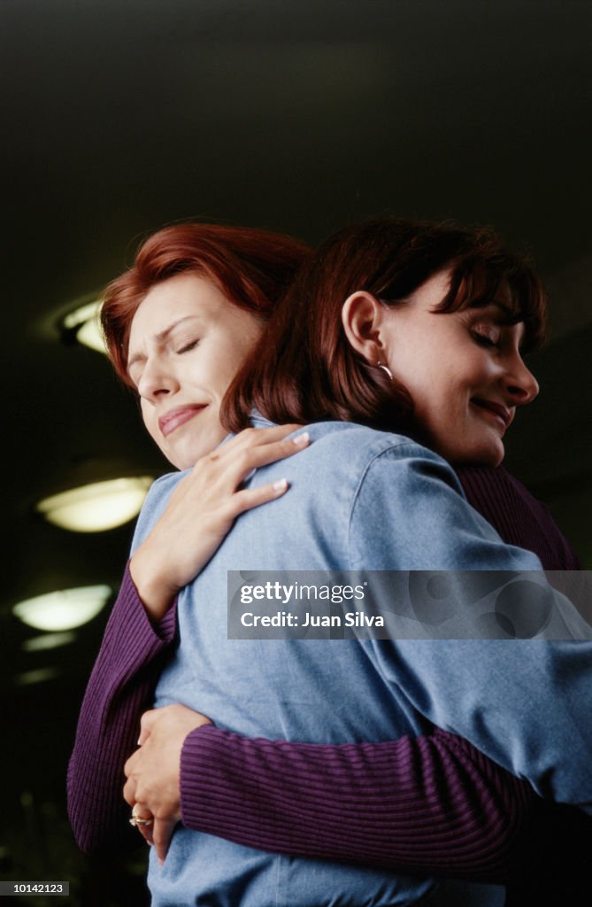 2 WOMEN HUG IN HOSPITAL WAITING ROOM