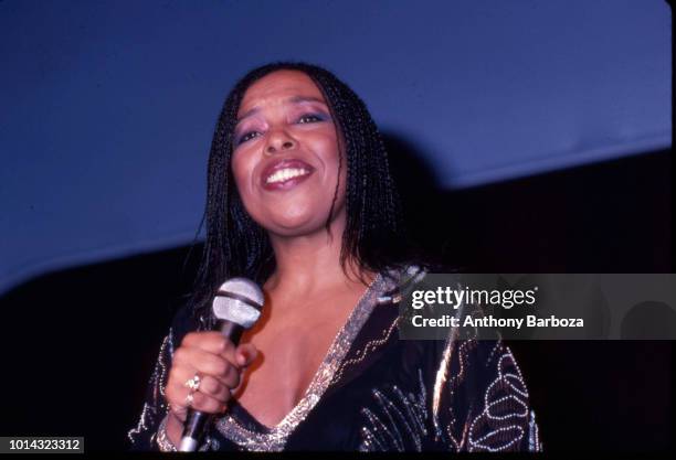 Low-angle view of Jazz and R&B musician Roberta Flack as she holds a microphone and smiles onstage, late twentieth century.