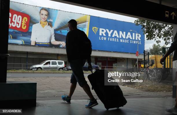 Man pulling a suitcase walks past a billboard advertisement for RyanAir during a 24-hour strike by RyanAir pilots on August 10, 2018 in Schoenefeld,...