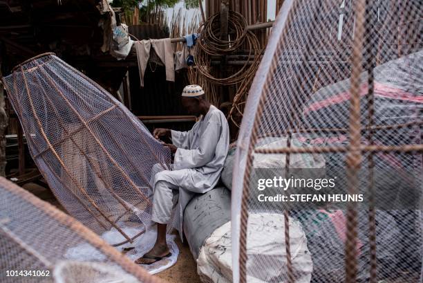 Man building fish traps is seen sowing a net onto a wooden frame in the Baga fish market in in Maiduguri on July 31, 2017. - The fish trade in Borno...