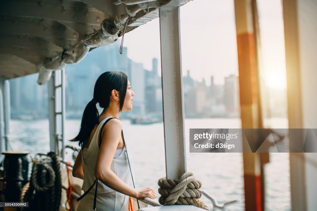 Young woman looking over the spectacular city skyline of Hong Kong at dusk while riding on Star Ferry