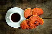 Cup of reishi tea and fresh Lingzhi mushroom on dark wooden floor.