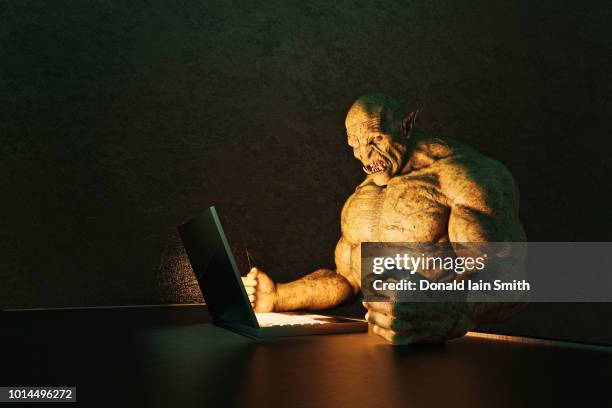internet troll: angry ogre pounding fists on desk while using laptop computer - ogre fictional character fotografías e imágenes de stock