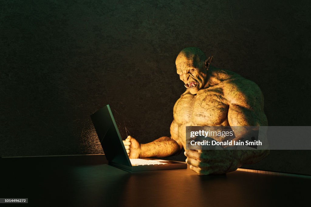 Internet troll: angry ogre pounding fists on desk while using laptop computer