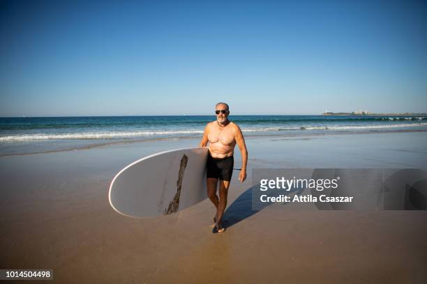 senior man with surfboard after surfing at beach - kayaking australia stock pictures, royalty-free photos & images