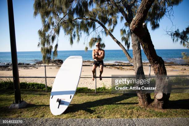 Smiling senior man sitting on fence at beach with surfboard