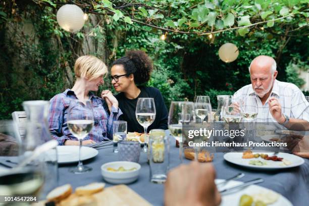lesbian couple holding hands at bbq with family - alte und junge lesbische frauen stock-fotos und bilder