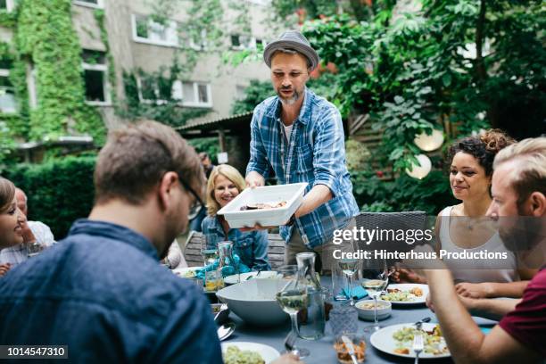 man dishing out food at bbq in courtyard - männer grillen stock-fotos und bilder