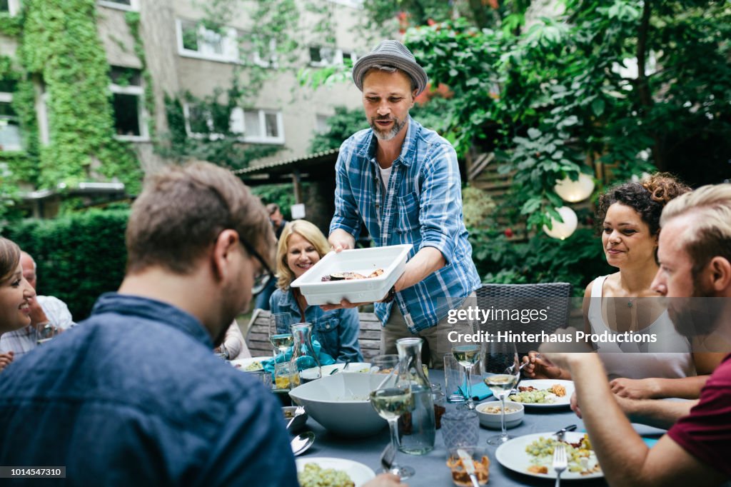 Man Dishing Out Food At BBQ In Courtyard