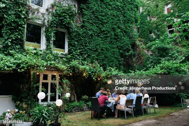 Family Sitting Down For Meal In Courtyard Together