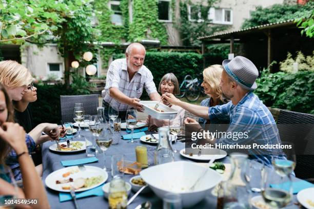 family sharing food at bbq in courtyard together - old man young woman stockfoto's en -beelden