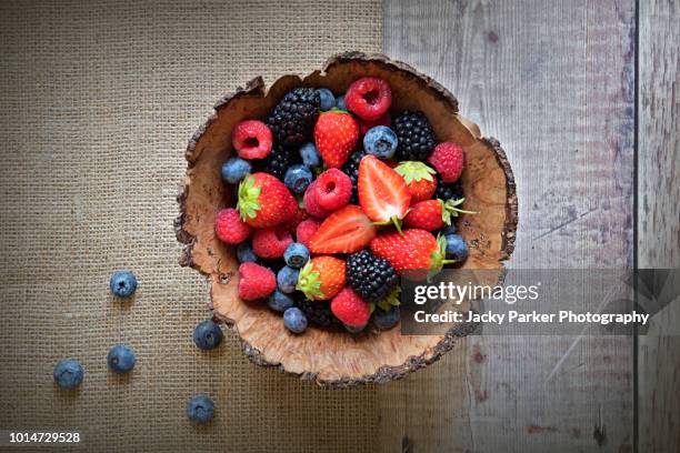 close-up image of a wooden bowl full of healthy summer berries including strawberries, raspberries, black berries and blue berries. - blueberries fruit fotografías e imágenes de stock