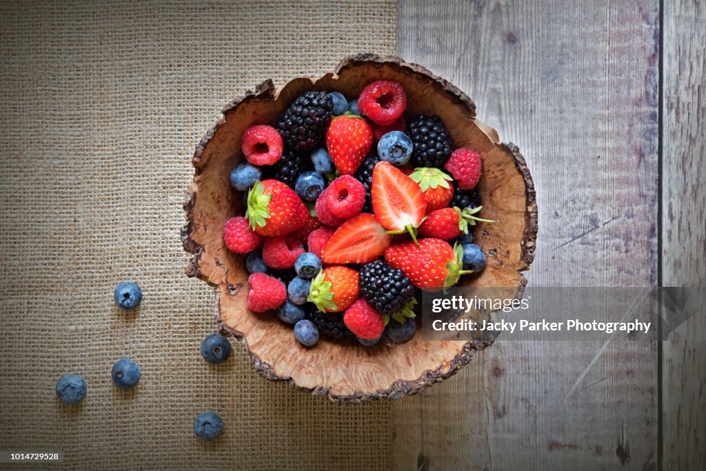 Close-up image of a wooden bowl full of Healthy Summer berries including Strawberries, raspberries, black berries and blue berries.