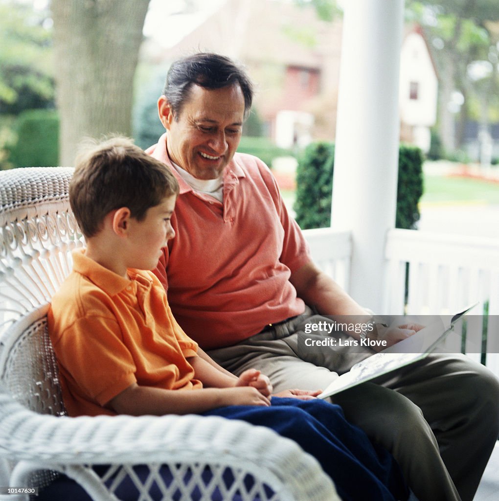 Grandfather and grandson reading book on porch