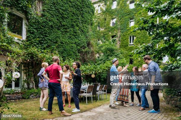 group of family members greeting one another before outdoor meal - garden party stock-fotos und bilder