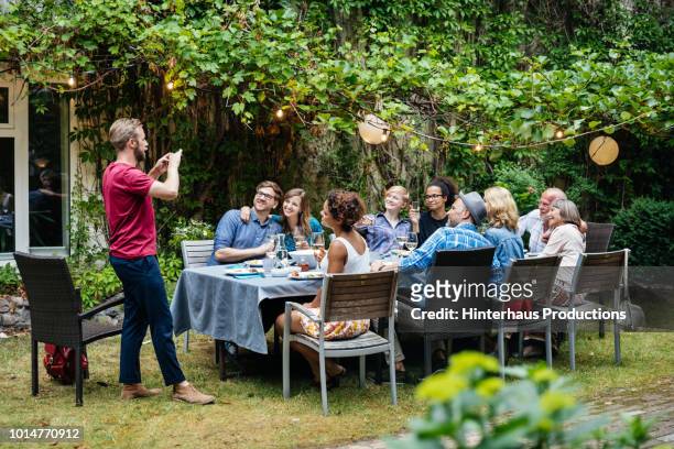 man taking photo of family having lunch outdoors - dinner party stock pictures, royalty-free photos & images