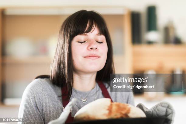 smiling woman standing in the kitchen holding a freshly baked loaf of bread - oler fotografías e imágenes de stock