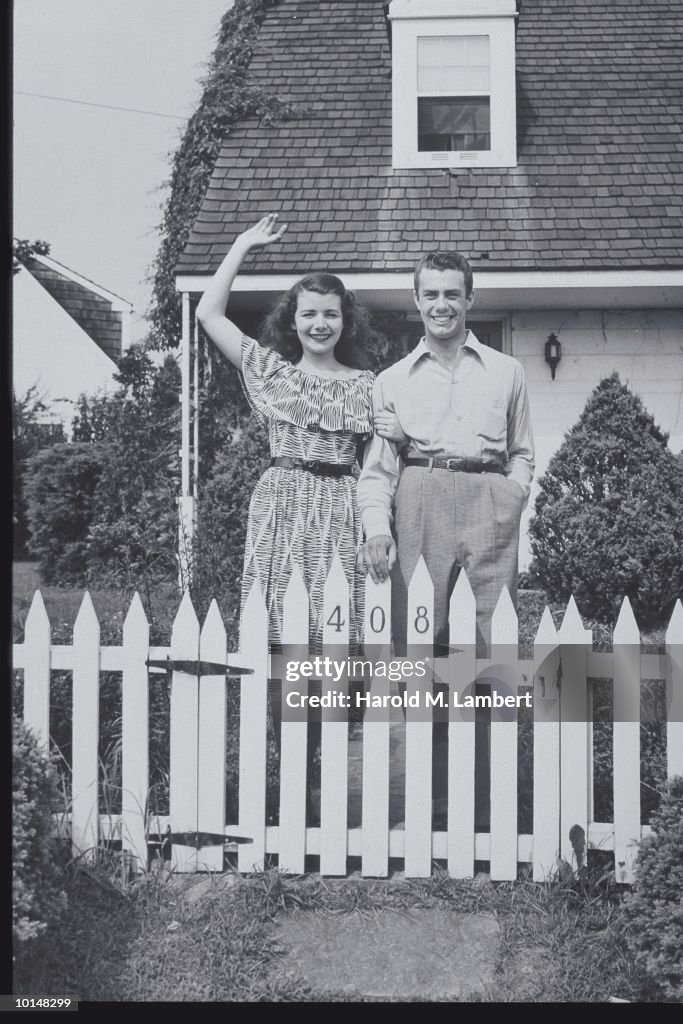 COUPLE WAVES BY WHITE PICKET FENCE, 1947, THE AMERICAN DREAM