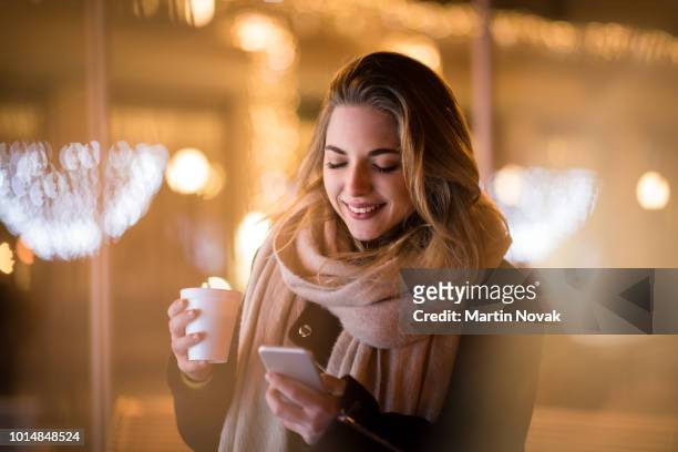 girl checks her phone while having coffee outside - christmas coffee stock-fotos und bilder