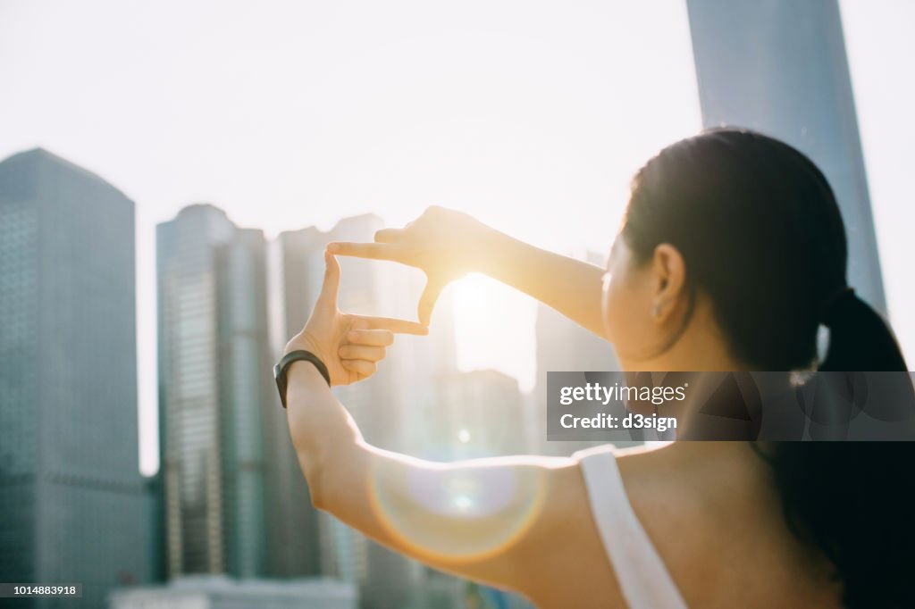 Rear view of young woman frames the Hong Kong city skyline into a finger frame under a sunny sky