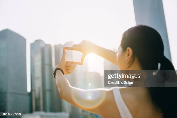 rear view of young woman frames the hong kong city skyline into a finger frame under a sunny sky - finger frame stock pictures, royalty-free photos & images