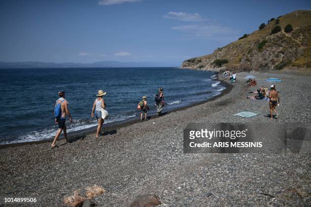 People walk on a beach near the village of Skala Sykamineas, on the Greek island of Lesbos, on August 3, 2018.