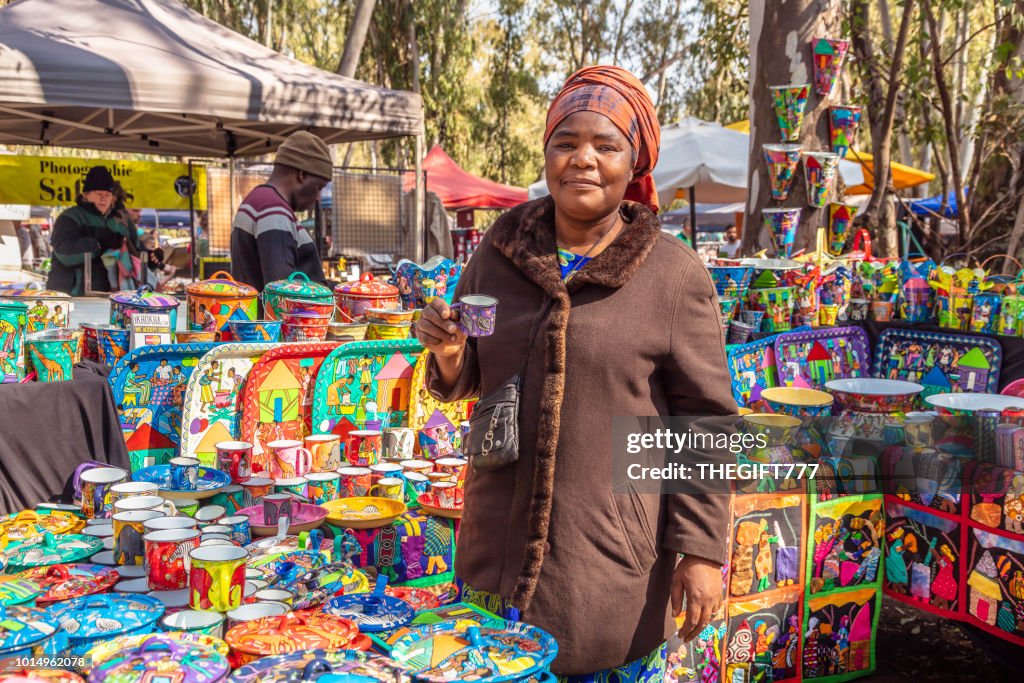 African vendor selling designs on metal cups at the Irene Market