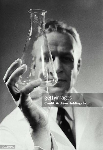 scientist examines a beaker, 1950s - bouteille d'erlenmeyer photos et images de collection