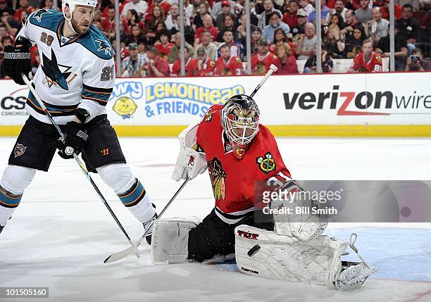 Goalie Antti Niemi of the Chicago Blackhawks reaches out to stop the puck as Ryane Clowe of the San Jose Sharks waits in position, at Game Four of...