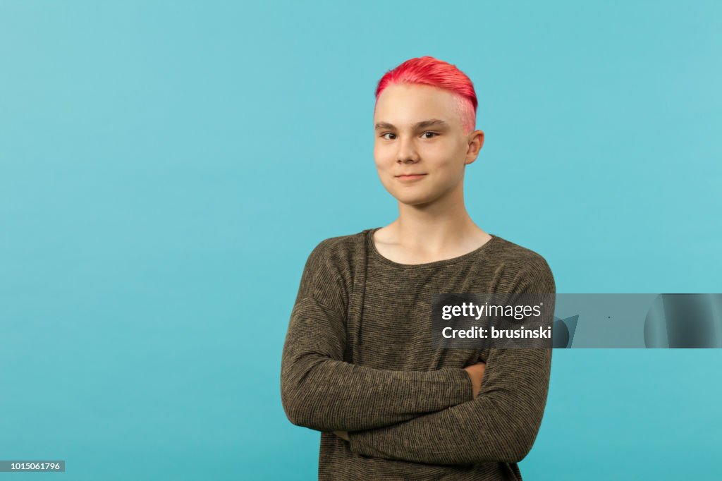 Portrait of a teenager boy with pink hair in the studio on a blue background