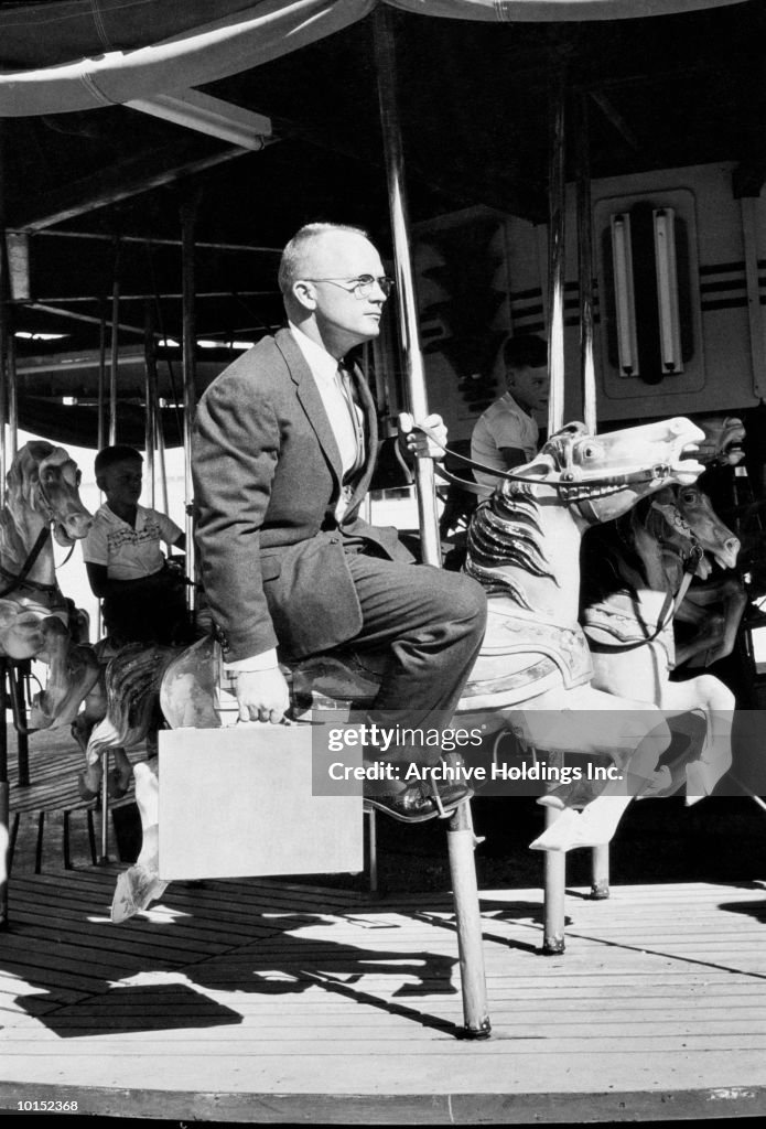 BUSINESSMAN RIDES ON A MERRY GO ROUND