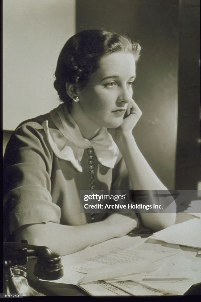 YOUNG WOMAN SEATED AT A DESK, CIRCA 1935