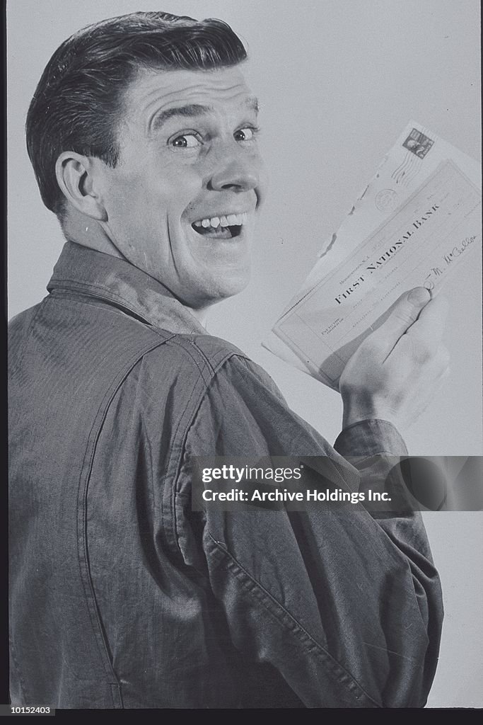 SMILING MAN HOLDING UP A CHECK, CIRCA 1950s