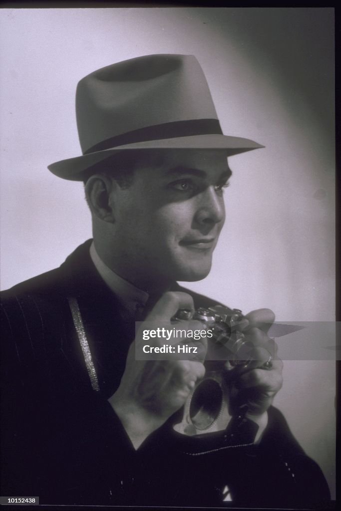 PHOTOGRAPHER WITH CAMERA AND HAT, 1930S