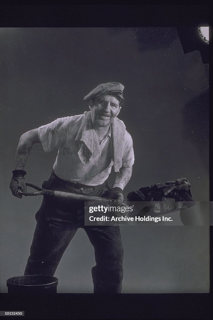 MAN IN WORK CLOTHES SHOVELS COAL, CIRCA 1930
