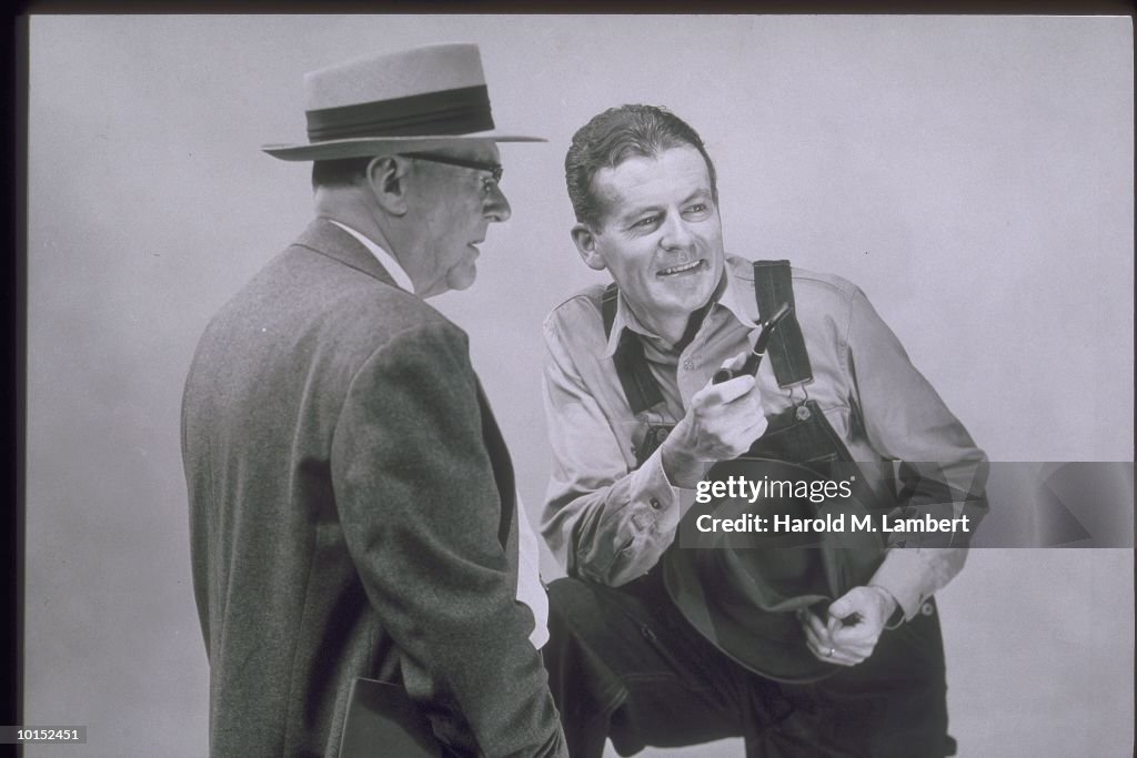 MAN IN OVERALLS TALKS TO MAN IN SUIT