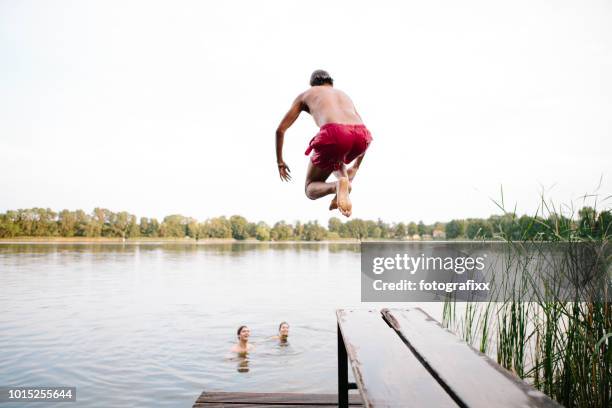 jour d’été : trois jeunes adultes sautent depuis la jetée dans le lac - ponton photos et images de collection