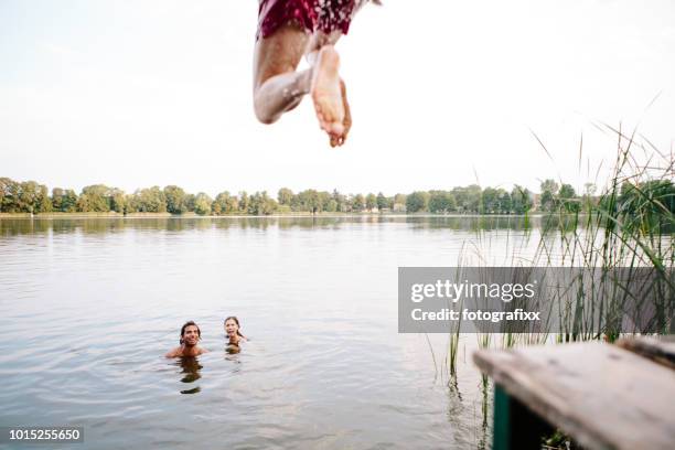 summer day: three young adults jump from jetty into lake - cannonball diving stock pictures, royalty-free photos & images