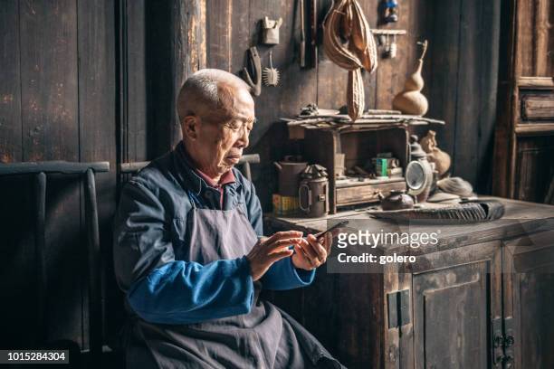 homem chinês sênior, tocando no celular em casa de madeira - folklore - fotografias e filmes do acervo