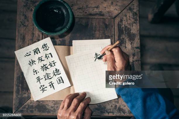 chinese senior man schrijven chinese kalligrafie tekens op papier - mandarijn stockfoto's en -beelden