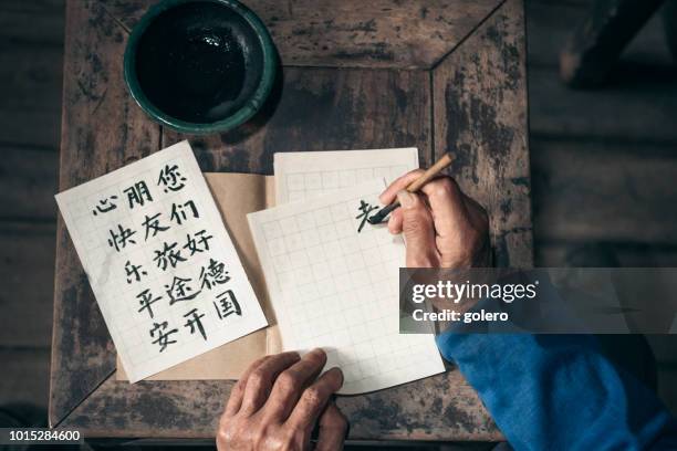 chinese senior man writing chinese calligraphy characters on paper - caligrafia imagens e fotografias de stock