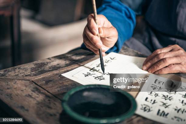 homme senior chinois écrire les caractères de la calligraphie chinoise sur papier - écriture chinoise photos et images de collection