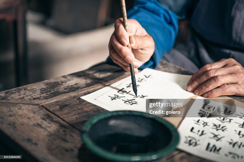 Chinese senior man writing chinese calligraphy characters on paper