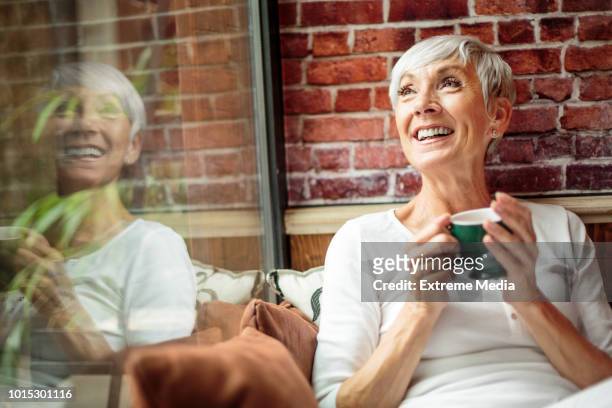portrait of smiling senior woman holding a cup in the cafeteria - old woman by window stock pictures, royalty-free photos & images