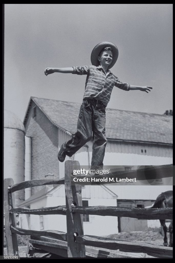 BOY BALANCING ON WOOD BEAM AT FARM, 1950S